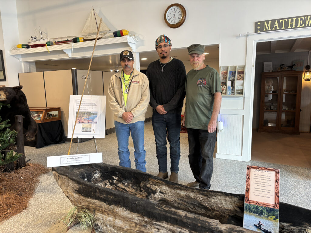 An exhibit celebrating early Mathews life and focusing on the indigenous population opened Saturday at the Mathews Museum. Among those on hand, from left, were R. Wayne Bowman of Gloucester, vice chief of the Kiskiack tribe; Zachary Yupo Thomas, president of the Native Student Club at Mary Washington University, Fredericksburg; and museum president Tom Robinson. They are standing in front of a canoe hand-hewn by historian Russell Reed of Onemo.